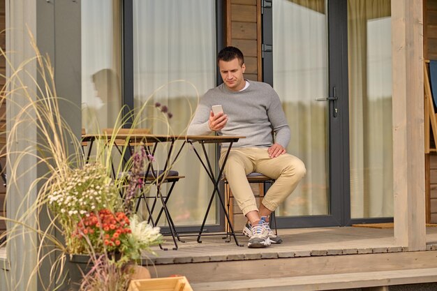 Homme assis à table près de la maison regardant un smartphone