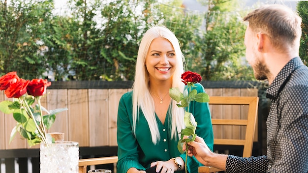 Homme assis sur le toit donnant rose rouge à sa petite amie souriante