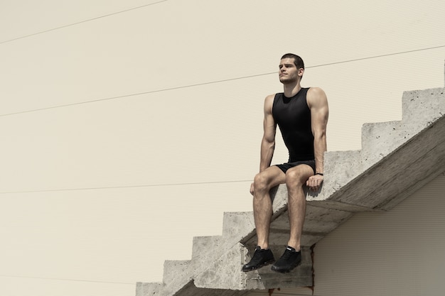 Homme athlétique assis sur des escaliers en béton ascendants
