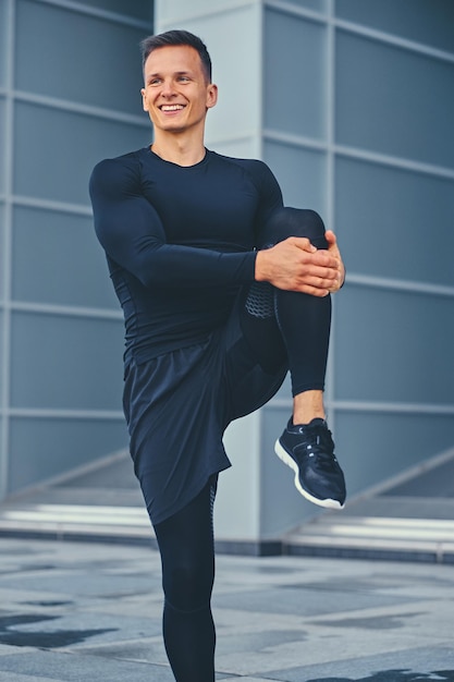 Un homme athlétique sportif s'échauffe et s'étire à l'extérieur sur fond de bâtiment moderne.