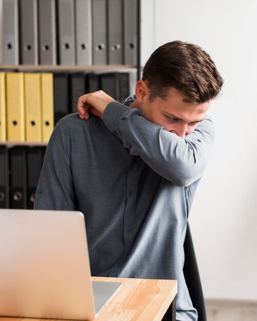 Homme au bureau lors d'une pandémie éternue dans son coude