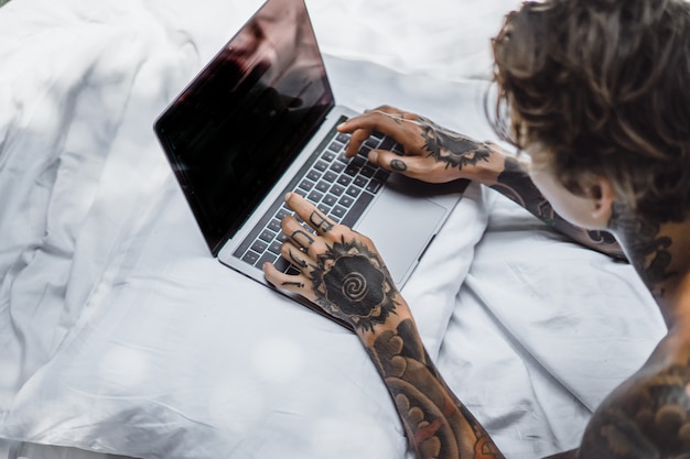 un homme au lit travaillant sur un ordinateur portable, vérifiant le courrier, regardant un film, écoutant de la musique