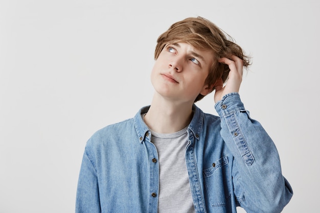 Homme aux cheveux blonds stupéfait aux yeux bleus, regarde avec une expression perplexe, essaie de se souvenir de quelque chose d'important. Jeune homme rêveur songeur pose à l'intérieur