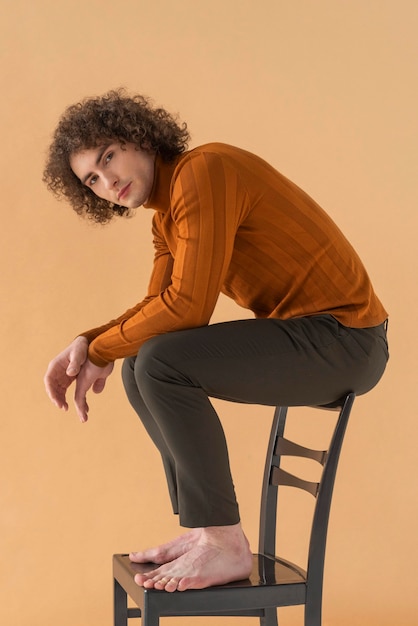 Homme aux cheveux bouclés avec chemisier marron posant sur une chaise