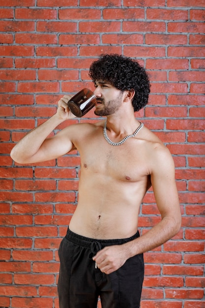 Homme aux cheveux bouclés à moitié nu buvant une tasse de thé.