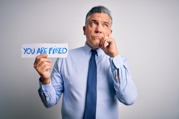 Photo gratuite homme aux cheveux gris d'âge moyen licencié avec des problèmes de tenue de papier avec vous êtes licencié message visage sérieux pensant à la question idée très confuse