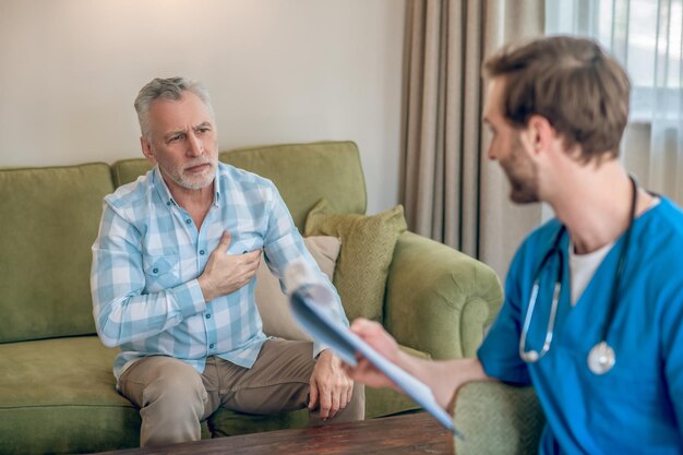 Photo gratuite homme aux cheveux gris bouleversé dans une chemise à carreaux se plaignant de sa douleur à la poitrine à un cardiologue