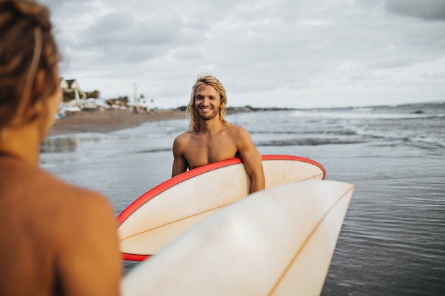 L'homme aux cheveux longs avec le sourire regarde la fille. Couple va surfer