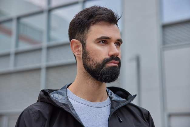 un homme aux cheveux noirs concentré dans la ditance pense à quelque chose vêtu d'une veste noire qui se promène dans la rue pendant la journée. Concept de personnes et de style de vie