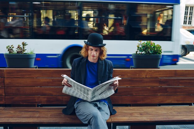 Homme aux cheveux rouges hipster assis sur un banc avec du papier journal