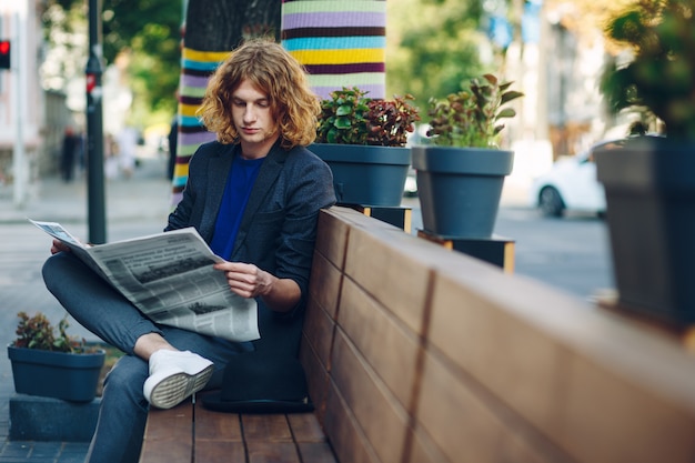 Photo gratuite homme aux cheveux rouges hipster assis sur un banc en lisant un journal