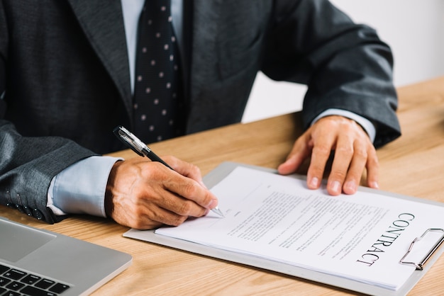 Homme avocat signant le contrat avec un stylo sur le presse-papiers