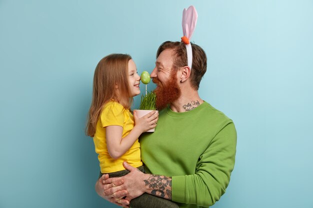 Homme à la barbe au gingembre portant des vêtements colorés et des oreilles de lapin tenant sa fille