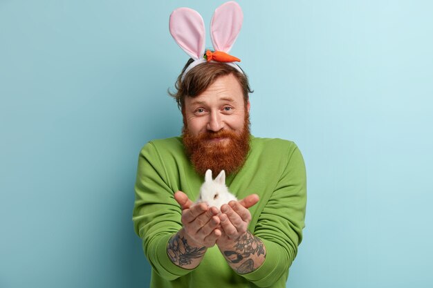 Homme avec barbe au gingembre portant des vêtements colorés et tenant un lapin