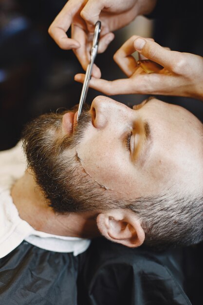 Homme avec une barbe. Coiffeur avec un client. Homme avec un peigne et des ciseaux