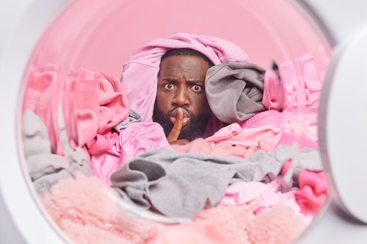 Photo gratuit l'homme à la barbe épaisse fait des corvées met les vêtements sales dans la machine à laver fait un geste de silence recouvert de lessive. photo prise depuis la laveuse. blanchisserie à la maison