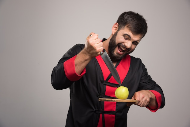 Homme à barbe essayant de couper une pomme sur une planche de bois.