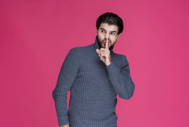 Homme à la barbe faisant signe de silence ou pointant un volume élevé.