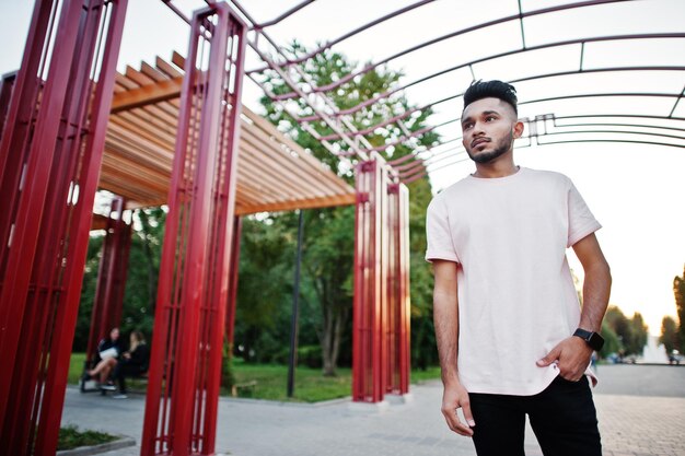 Homme de barbe indien élégant au t-shirt rose Modèle indien posé sous une arche rouge au parc de la ville