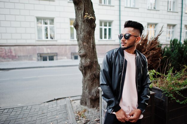 Homme de barbe indien élégant à la veste en cuir noir et lunettes de soleil Modèle indien posé en plein air dans les rues de la ville