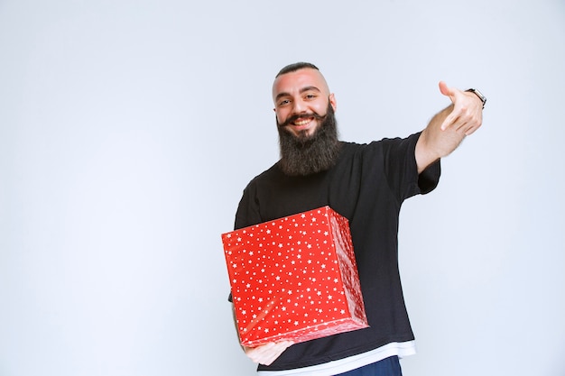 Homme à la barbe montrant sa boîte cadeau rouge.