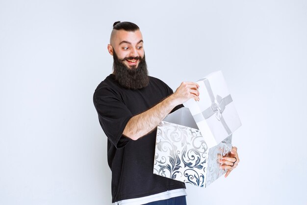 Homme à la barbe ouvrant une boîte cadeau blanche et souriant.