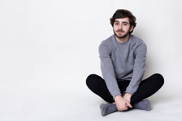 Un homme avec une barbe sombre et une moustache ayant une coiffure à la mode portant un pantalon décontracté