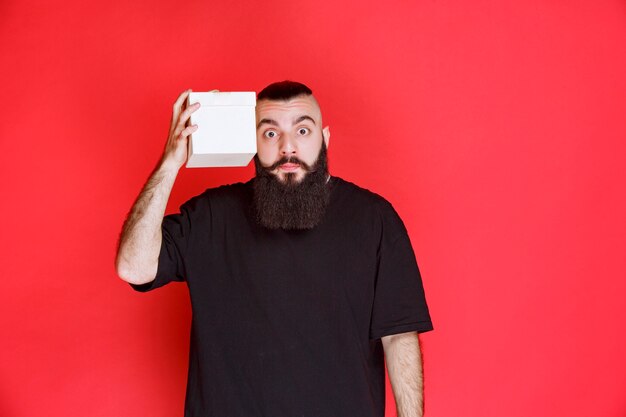 Homme à la barbe tenant une boîte-cadeau blanche et semble douteux de ce qu'il y a à l'intérieur.