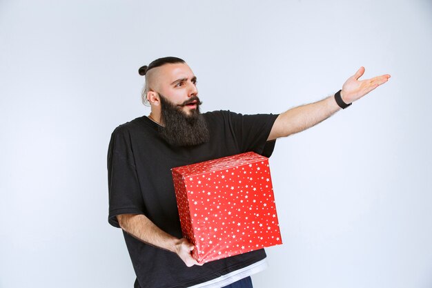 Homme à la barbe tenant une boîte-cadeau rouge et se disputant avec quelqu'un.