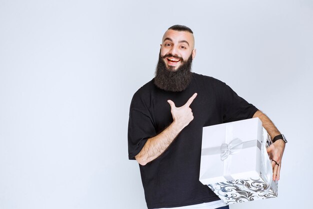 Homme à la barbe tenant un coffret cadeau bleu blanc souriant et se sentant heureux.