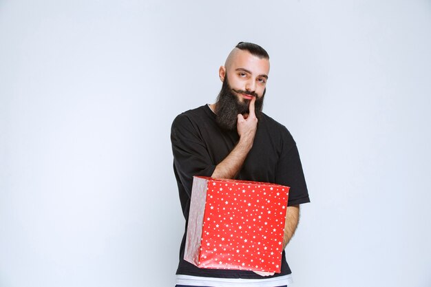 Homme à la barbe tenant des coffrets cadeaux rouges et hésitant à faire un choix.