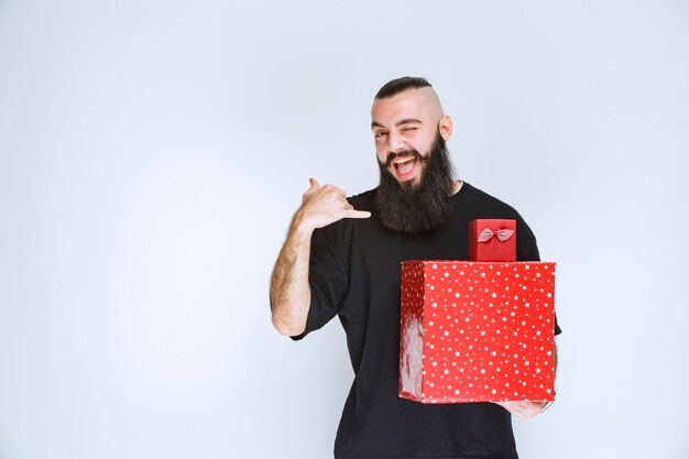 Homme à la barbe tenant des coffrets cadeaux rouges et pointant derrière.