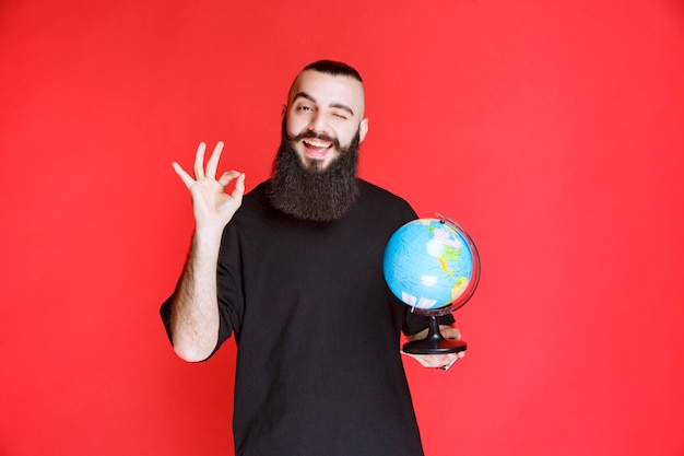 Photo gratuite homme à la barbe tenant un globe terrestre et en profitant.