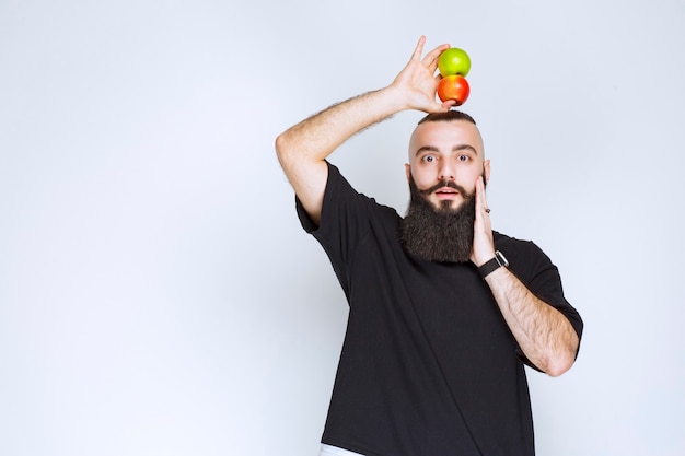 Homme à la barbe tenant des pommes au-dessus de sa tête.