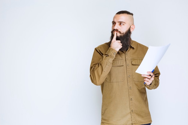 Homme à la barbe tenant un questionnaire et a l'air confus et réfléchi.