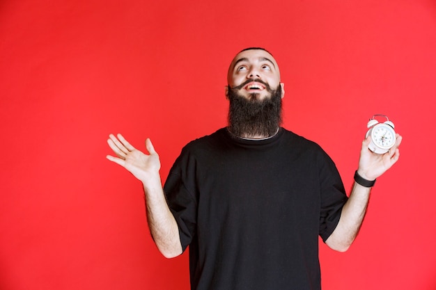 Homme à la barbe tenant un réveil et profitant du produit.