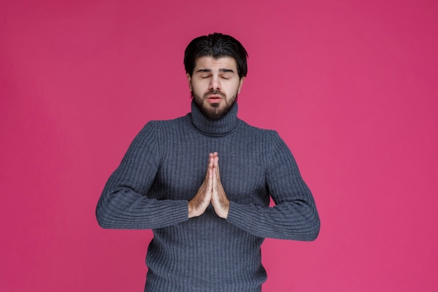 Homme à la barbe tenant ses mains d'une manière comme s'il prie ou souhaite quelque chose.