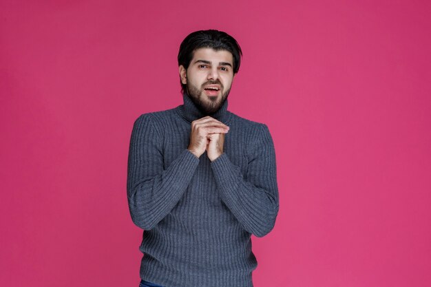 Homme à la barbe tenant ses mains d'une manière comme s'il prie ou souhaite quelque chose.