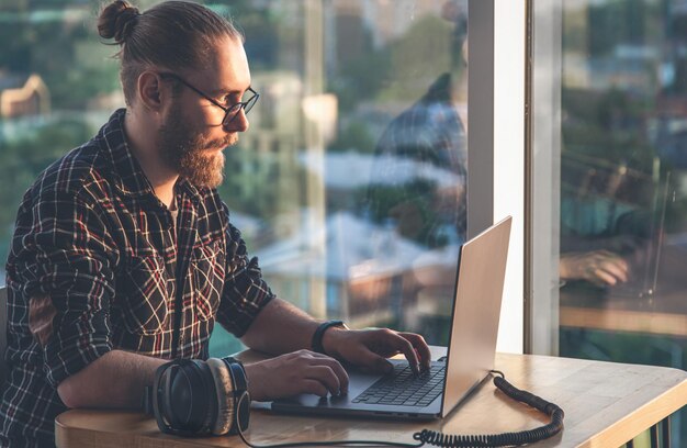 Un homme avec une barbe travaille devant un ordinateur assis dans le bureau près de la fenêtre