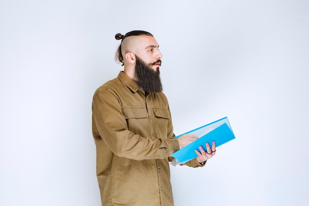 Homme à la barbe vérifiant la liste des projets et marquant des notes ou des corrections.