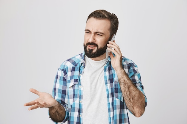 Un homme barbu adulte confus a une conversation téléphonique