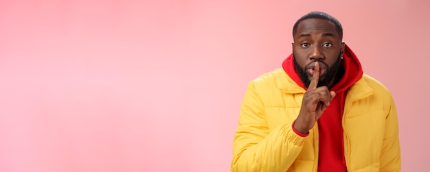 Homme barbu afro-américain à la taille sérieuse en veste jaune à capuche rouge plier l'appareil photo demandant ke