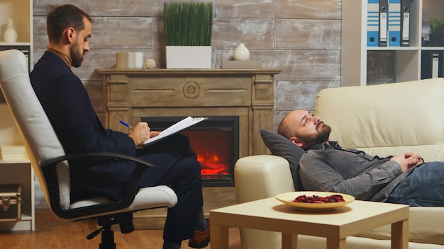 Photo gratuite homme barbu allongé sur un canapé lors d'une thérapie de couple parlant de ses conflits relationnels avec sa femme.