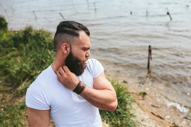 L'homme barbu américain regarde sur la rive du fleuve dans une veste bleue