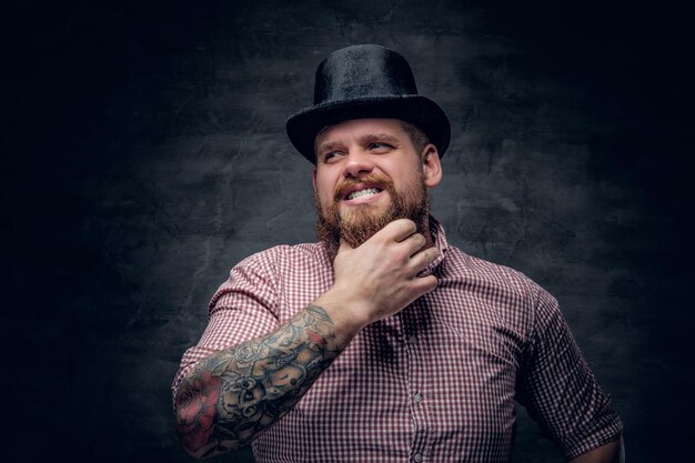 Homme barbu aux bras tatoués portant un chapeau haut de forme.