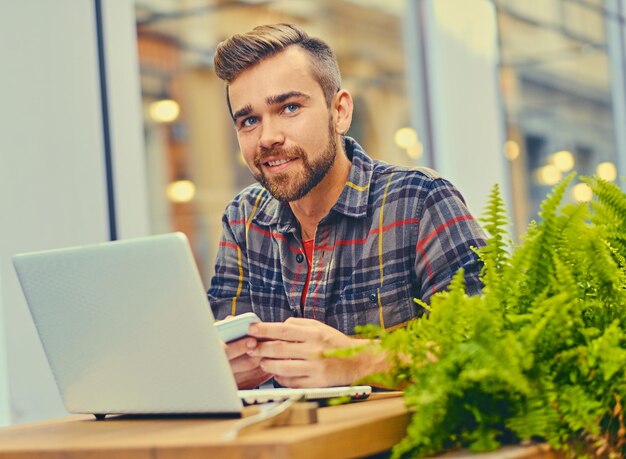 Homme barbu aux yeux bleus utilisant un ordinateur portable dans un café dans la rue.