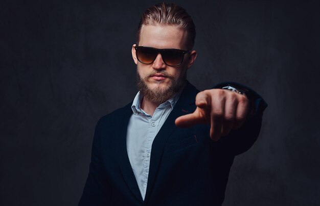 Un homme barbu blond élégant vêtu d'un costume et de lunettes de soleil.