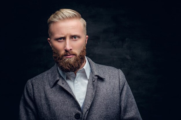 Homme barbu blond sérieux dans une chemise blanche et une veste classique et élégante sur fond sombre.