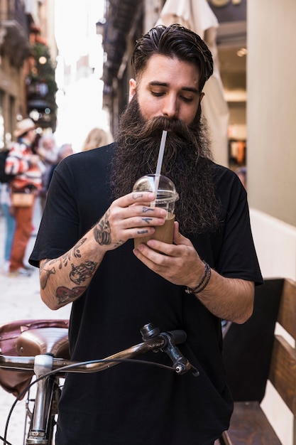Homme barbu buvant une boisson au chocolat debout avec vélo sur la rue