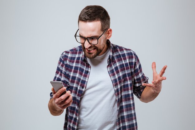 Homme barbu en colère dans des lunettes en regardant téléphone